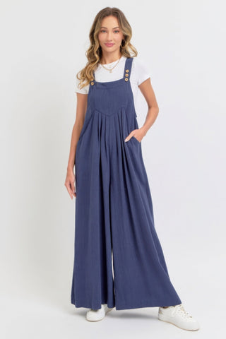 Woman wearing an adjustable strap overall wide leg jumpsuit in navy, featuring a chic and relaxed silhouette with a casual white t-shirt.