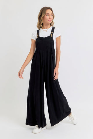 Woman wearing chic adjustable strap overall wide leg jumpsuit in black, showcasing relaxed modern style with white sneakers.
