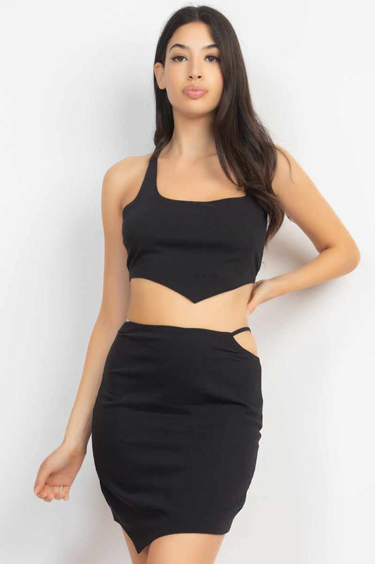 Woman wearing asymmetrical cross-back top and skirt set in black with scoop neckline and side cutouts.