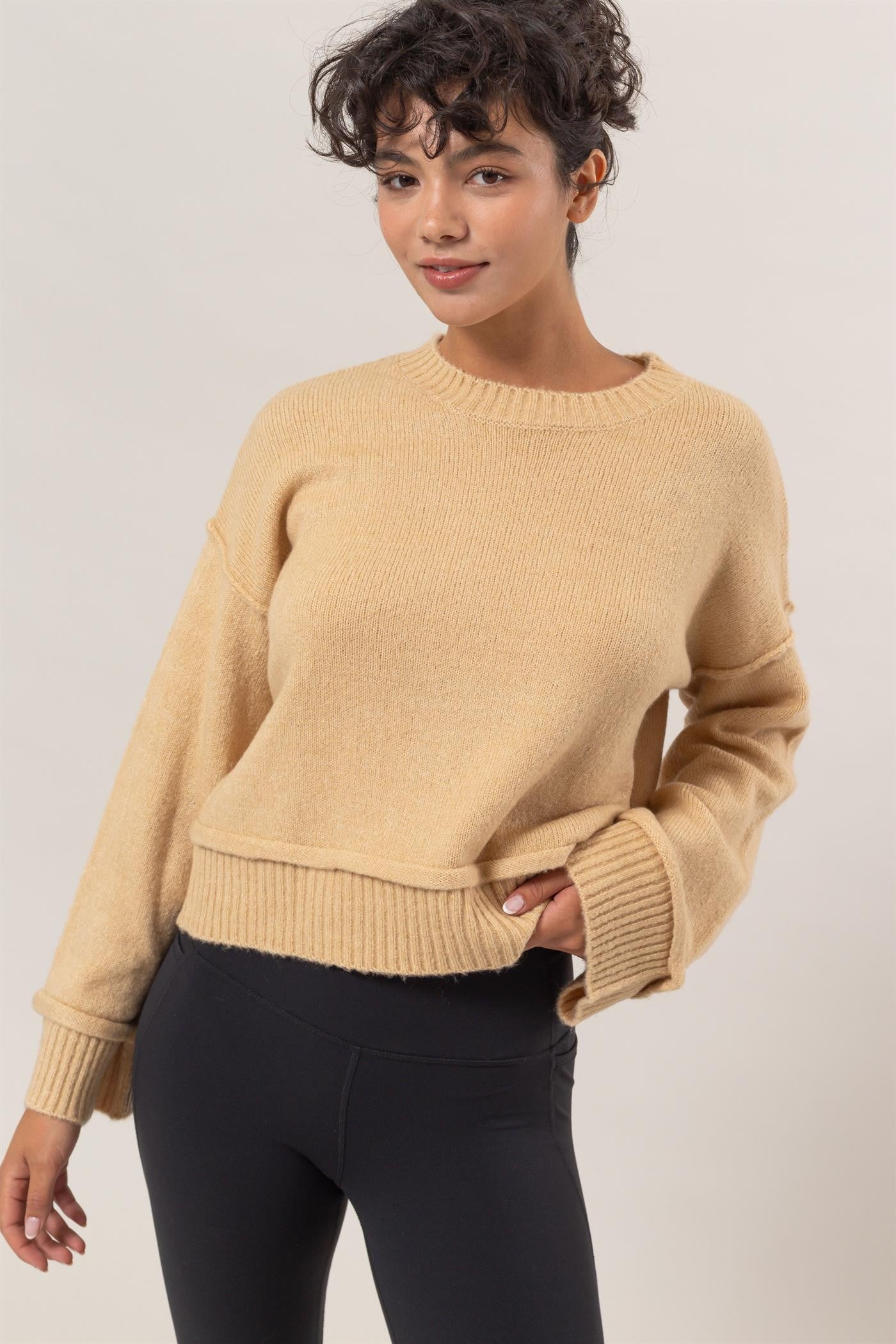 Woman wearing HYFVE Round Neck Dropped Shoulder Ribbed Sweater in beige, showcasing its relaxed, stylish fit and ribbed texture.