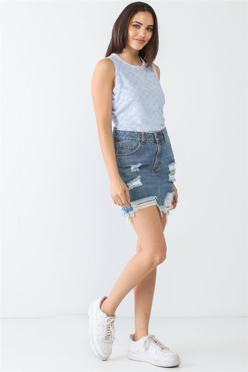 Woman wearing a sleeveless baby blue top with denim shorts and white sneakers, posing against a white background.