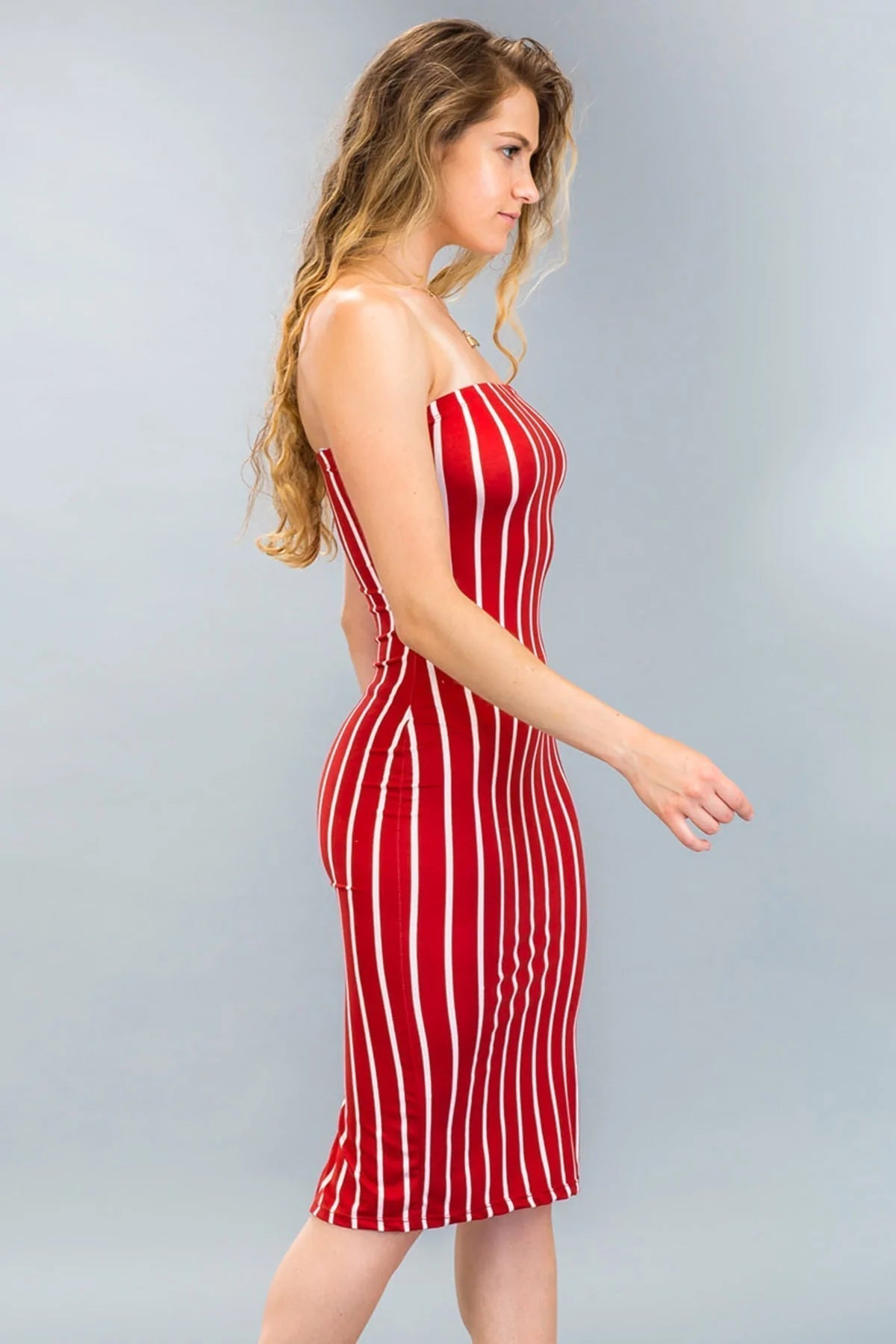 Woman wearing red striped back cut-out tube midi dress, side view, showcasing open shoulder design.