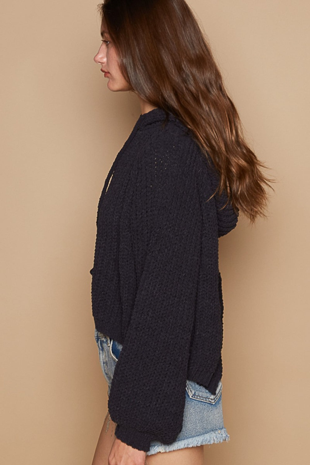 Woman wearing a back open slit balloon sleeve crop hooded sweater with denim shorts, side view.