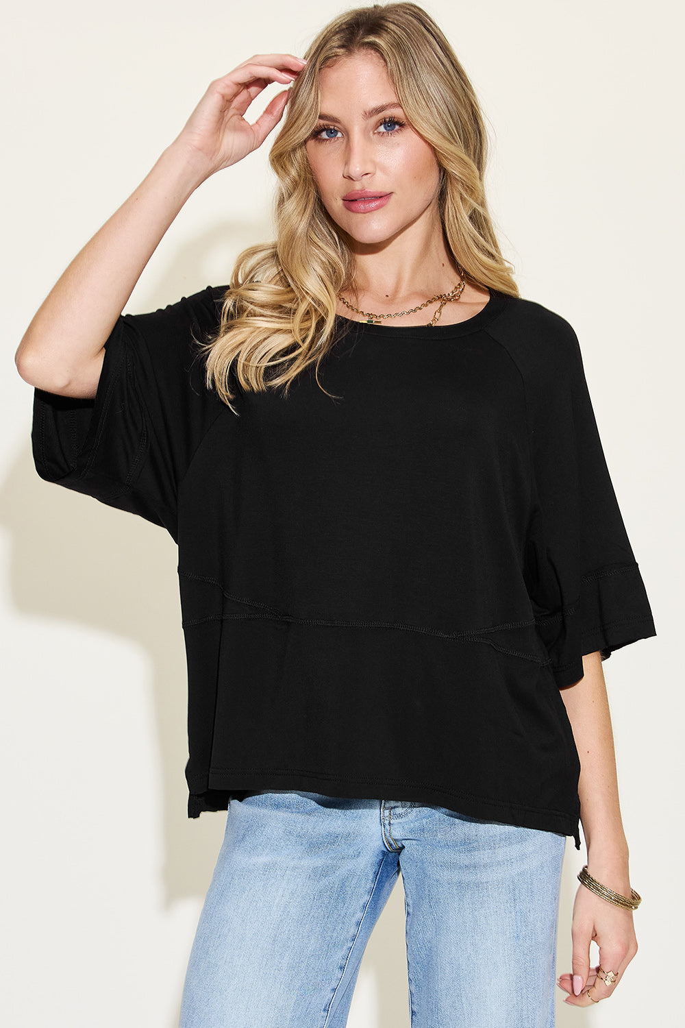 Woman wearing a black bamboo round neck exposed seam t-shirt with blue jeans, showcasing casual style and comfort.