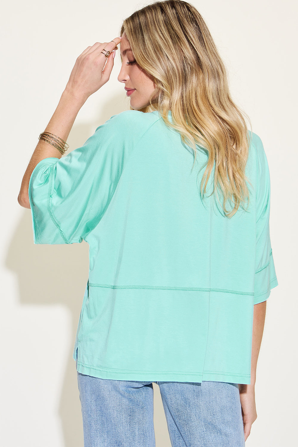 Woman wearing bamboo round neck exposed seam t-shirt in mint green, soft fabric with a relaxed fit and back view.