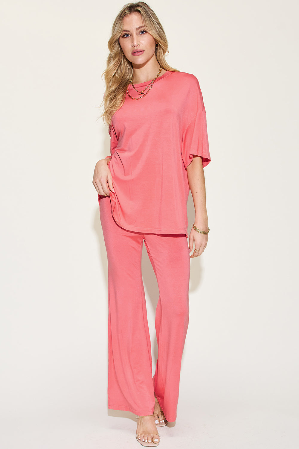 Woman wearing bamboo drop shoulder T-shirt and flare pants set in coral pink, showcasing basic style and stretchy, eco-friendly fabric.