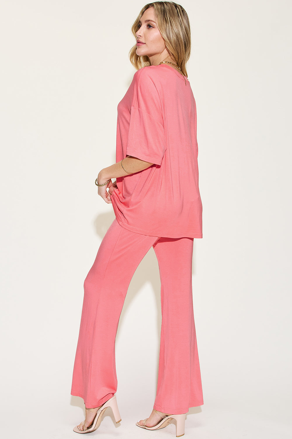 Woman wearing pink bamboo drop shoulder T-shirt and flare pants set, showcasing a comfortable and stylish basic outfit.