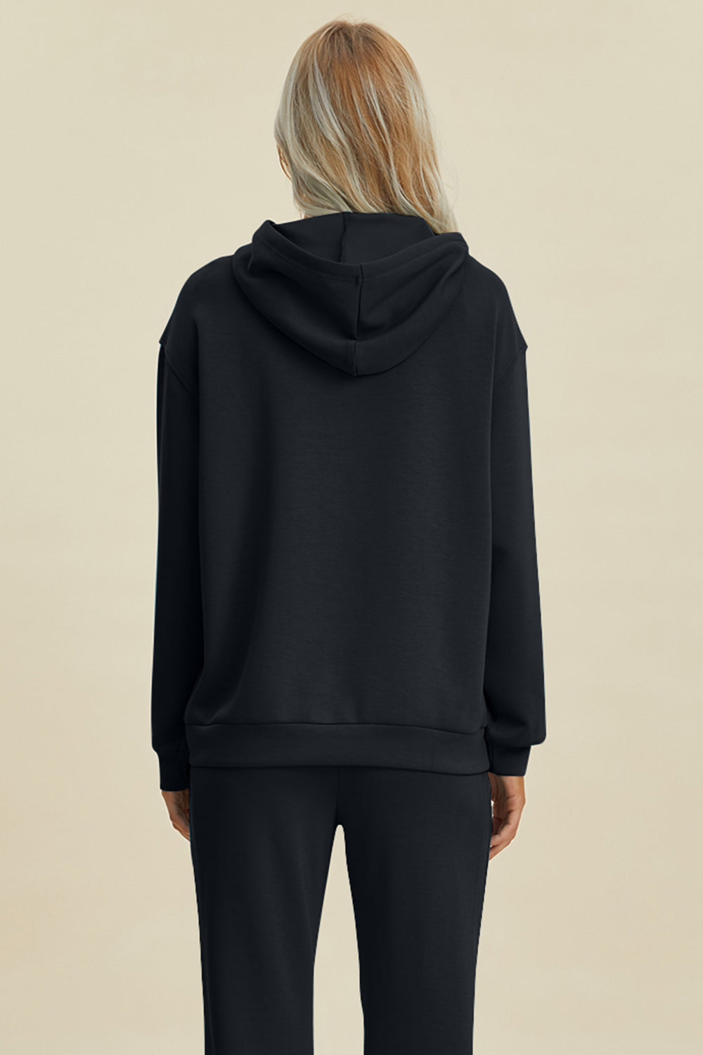 Woman wearing black hoodie with kangaroo pocket and drawstring, back view, made of rayon, polyester, and spandex blend.