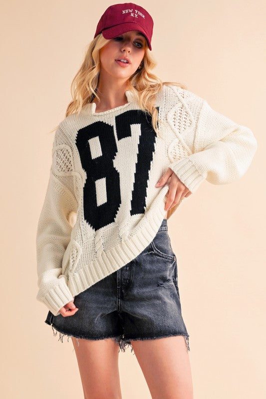 Woman wearing white contrast number cable knit drop shoulder sweater with exposed seam and ribbed details.