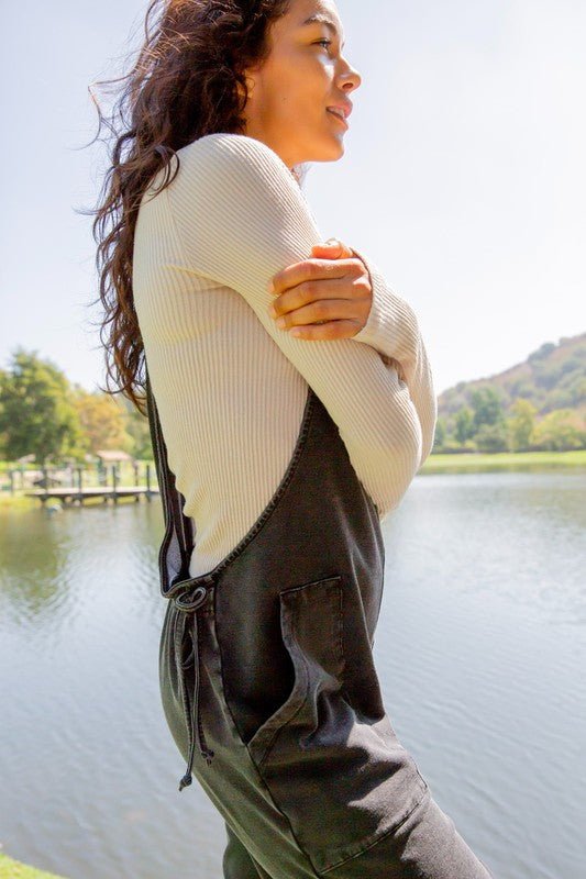Woman wearing black drawstring waist spaghetti strap overalls with pockets, standing by a lake.