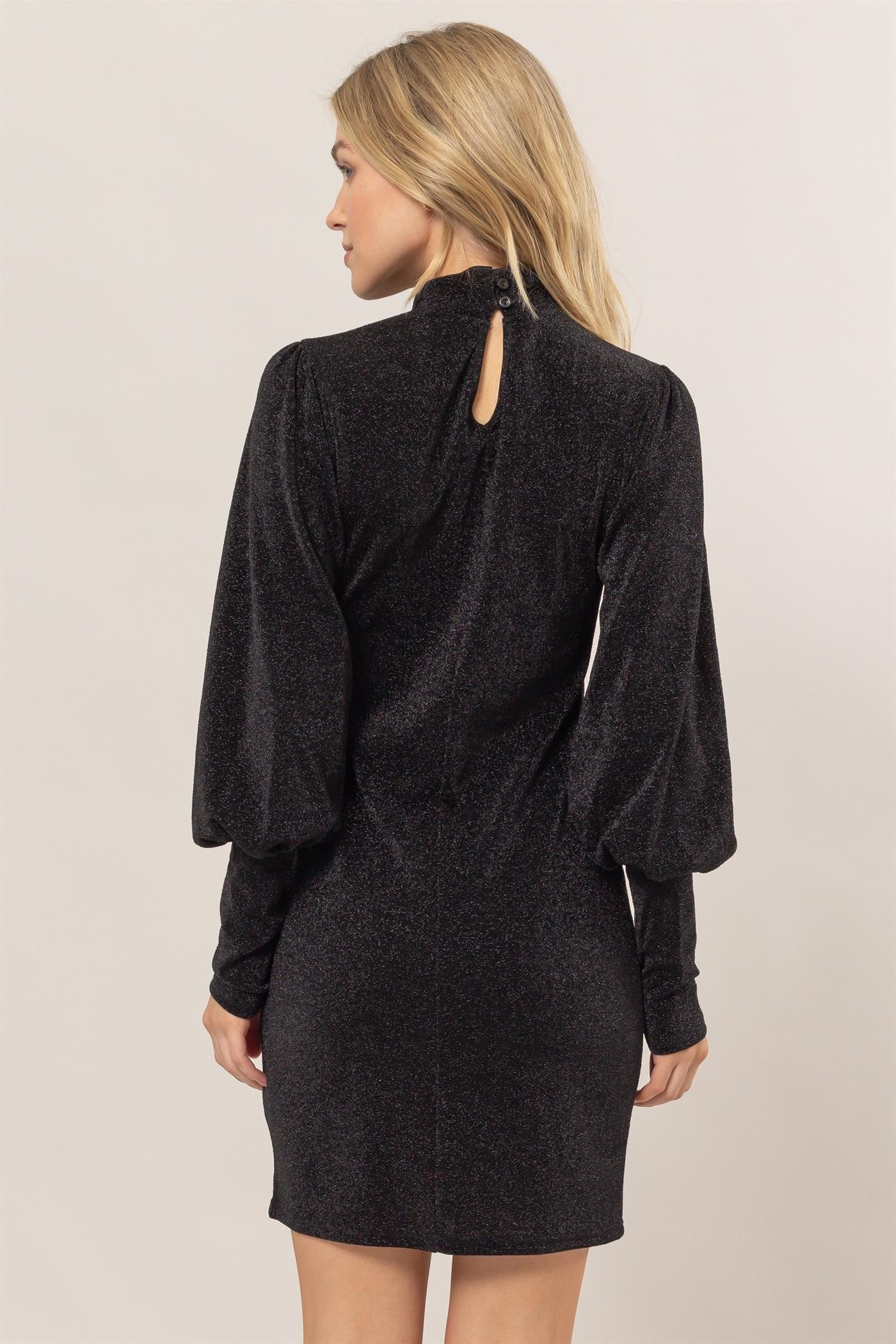 Woman wearing black glitter mock neck long sleeve mini dress with slightly stretchy fabric, shown from the back.