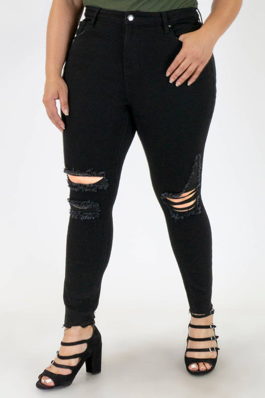 Plus size black skinny jeans with knee destruction, raw hem, 12" high rise, and 27" inseam, paired with strappy heels.