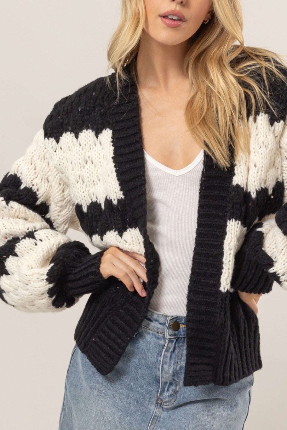 Woman wearing a black scallop striped open front cardigan with long sleeves and white top.