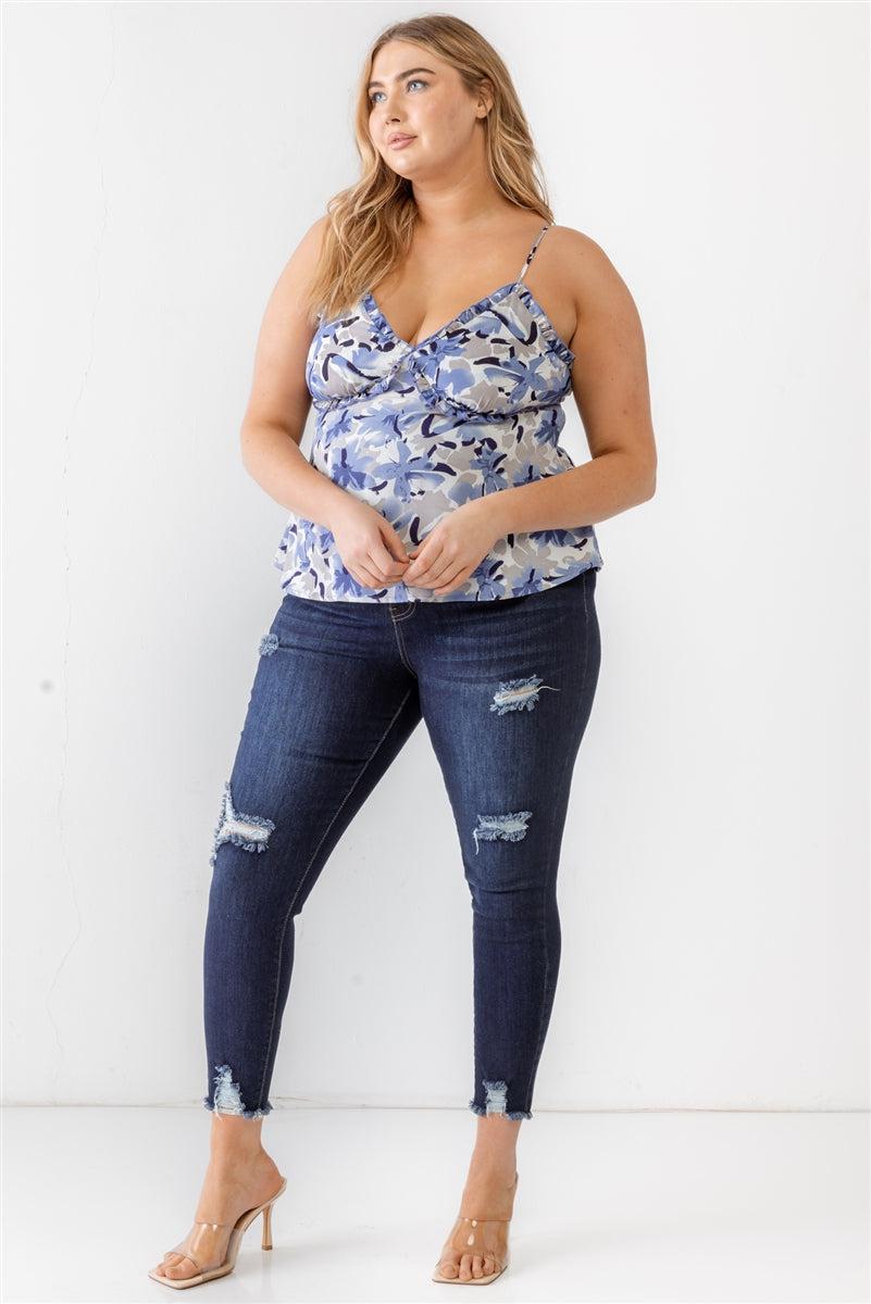 Plus size woman wearing a floral print blue woven tank top with ruffle detail, v-neckline, and adjustable straps paired with ripped jeans.