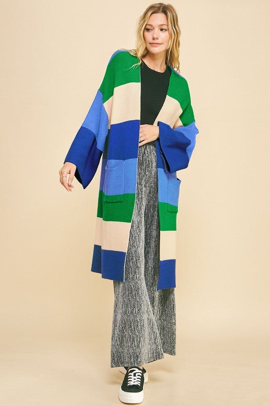 Woman wearing blue stripe color block kimono sleeve open front cardigan with pockets, styled casually with sneakers and wide-leg pants.