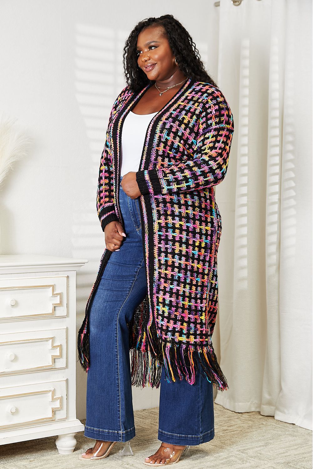 Woman wearing a multicolored fringe hem cardigan, paired with jeans for a bohemian chic look, perfect for versatile styling.