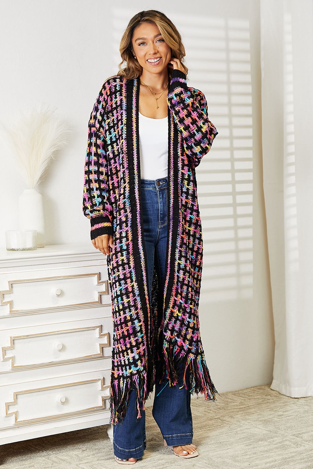 Woman wearing a bohemian chic multicolored open front cardigan with fringe hem, styled with jeans and a white top, perfect for layering.