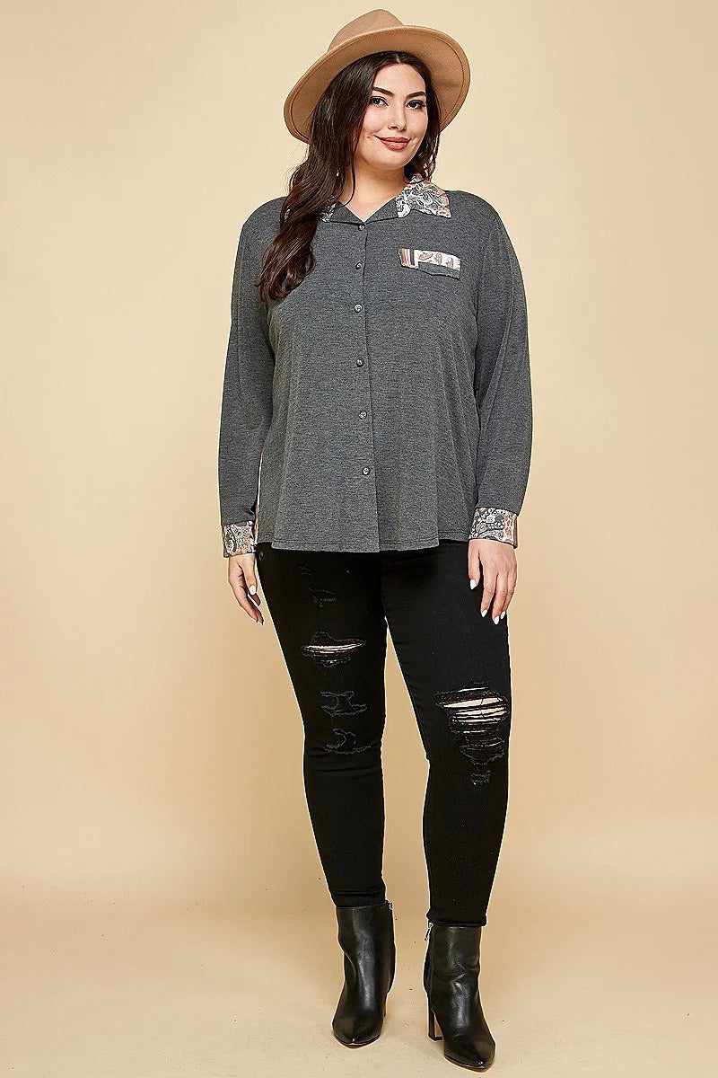 Plus size woman wearing charcoal printed patchwork contrast button-up shirt with faux pocket and black distressed jeans.