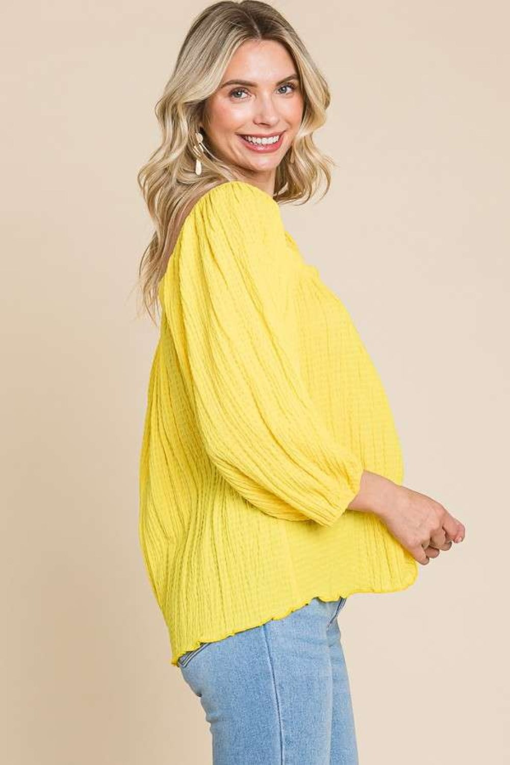 Woman wearing a yellow textured puff sleeve blouse with light blue jeans, showcasing a casual and stylish look.