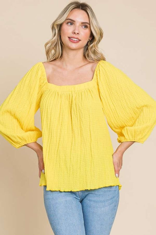 Woman wearing yellow square neck puff sleeve top with a flattering fit and ruched details, paired with jeans.