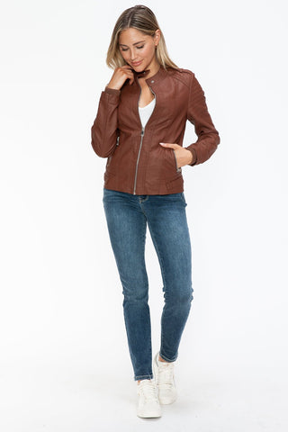 Woman wearing a Brandy PU leather biker jacket with side zip pockets, styled with blue jeans and white sneakers.