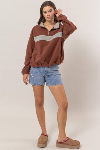 Woman wearing brick fleece color block half zip sweatshirt with denim shorts and slippers, showcasing casual style and comfort.
