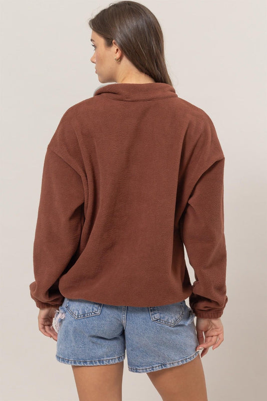 Woman wearing brick fleece color block half zip sweatshirt with casual denim shorts, viewed from the back.