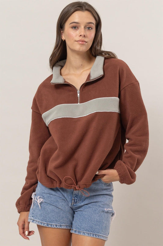 Woman wearing brick fleece color block half zip sweatshirt with denim shorts, showcasing stylish comfort and a unique design.