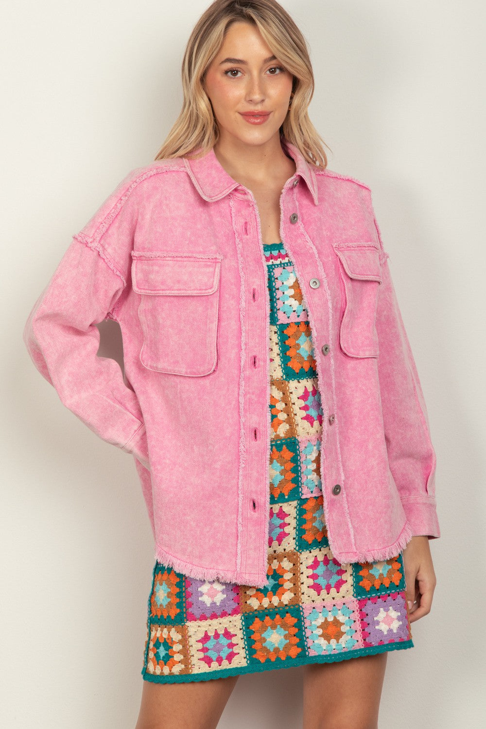 Woman wearing a pink button-up raw hem long sleeve jacket over a colorful dress, highlighting casual style and rayon-spandex blend fabric.