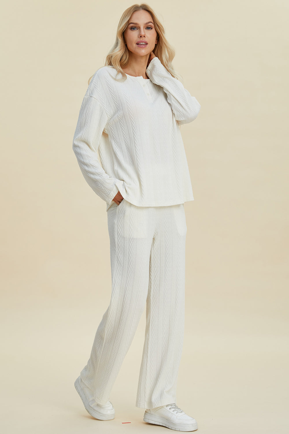 Woman wearing a white cable-knit long sleeve top and pants set, featuring button accents, slightly stretchy polyester-spandex blend.