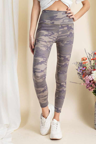 Woman wearing olive camouflage-printed rayon spandex leggings with a mid-rise fit, paired with white sneakers and a casual top.