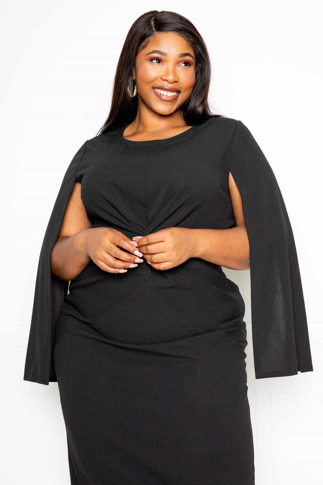 Plus size woman wearing a black cape sleeve dress with knot detail, available in 1XL, 2XL, and 3XL.