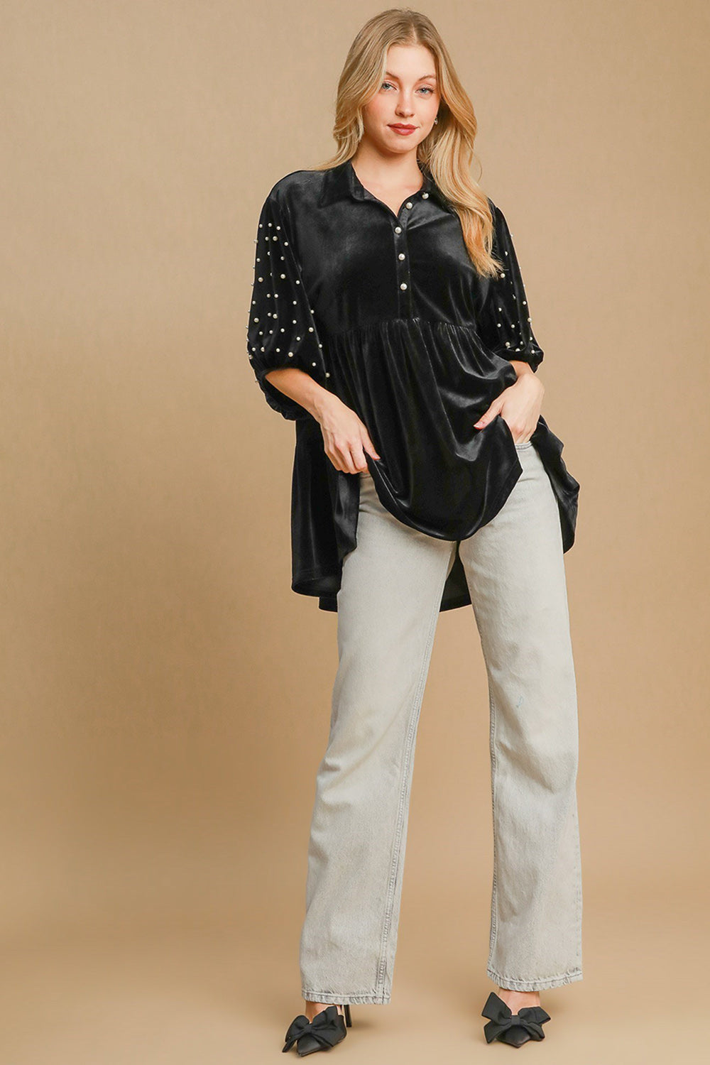 Woman wearing black pearl detail velvet babydoll blouse with tiered design and buttoned high-low hem.