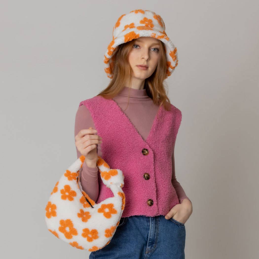 Woman wearing a winter flower pattern sherpa bucket hat and matching bag with floral print, pink vest, and jeans.