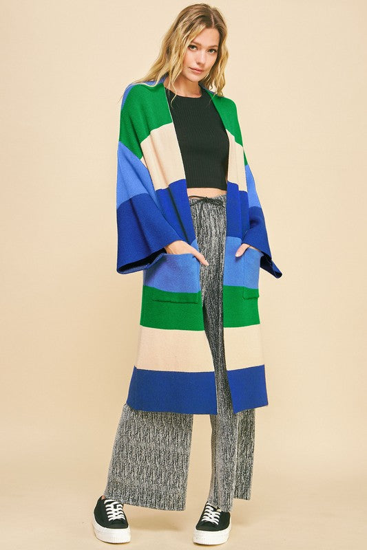 Woman wearing blue stripe color block kimono sleeve open front cardigan with pockets, paired with gray pants.