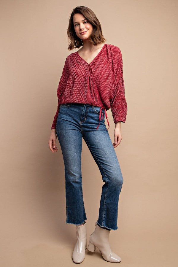 Woman wearing satin burgundy pleated drawstring top with snap button, paired with jeans and white ankle boots.