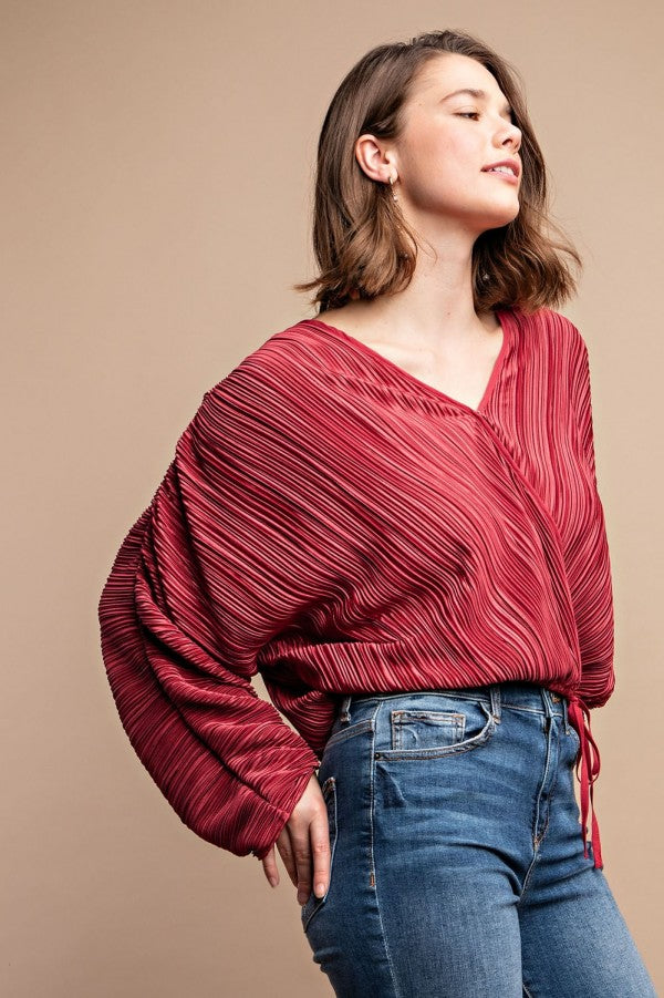 Woman wearing satin burgundy pleated drawstring top with snap button, adding chic and sophisticated style to her outfit.