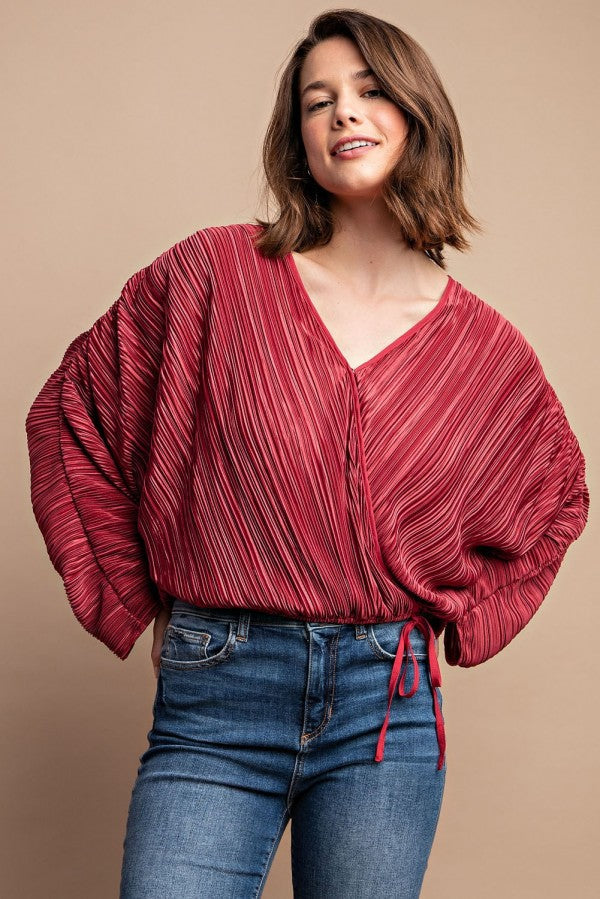 Woman wearing satin burgundy pleated drawstring top with snap button, showcasing chic and contemporary style.