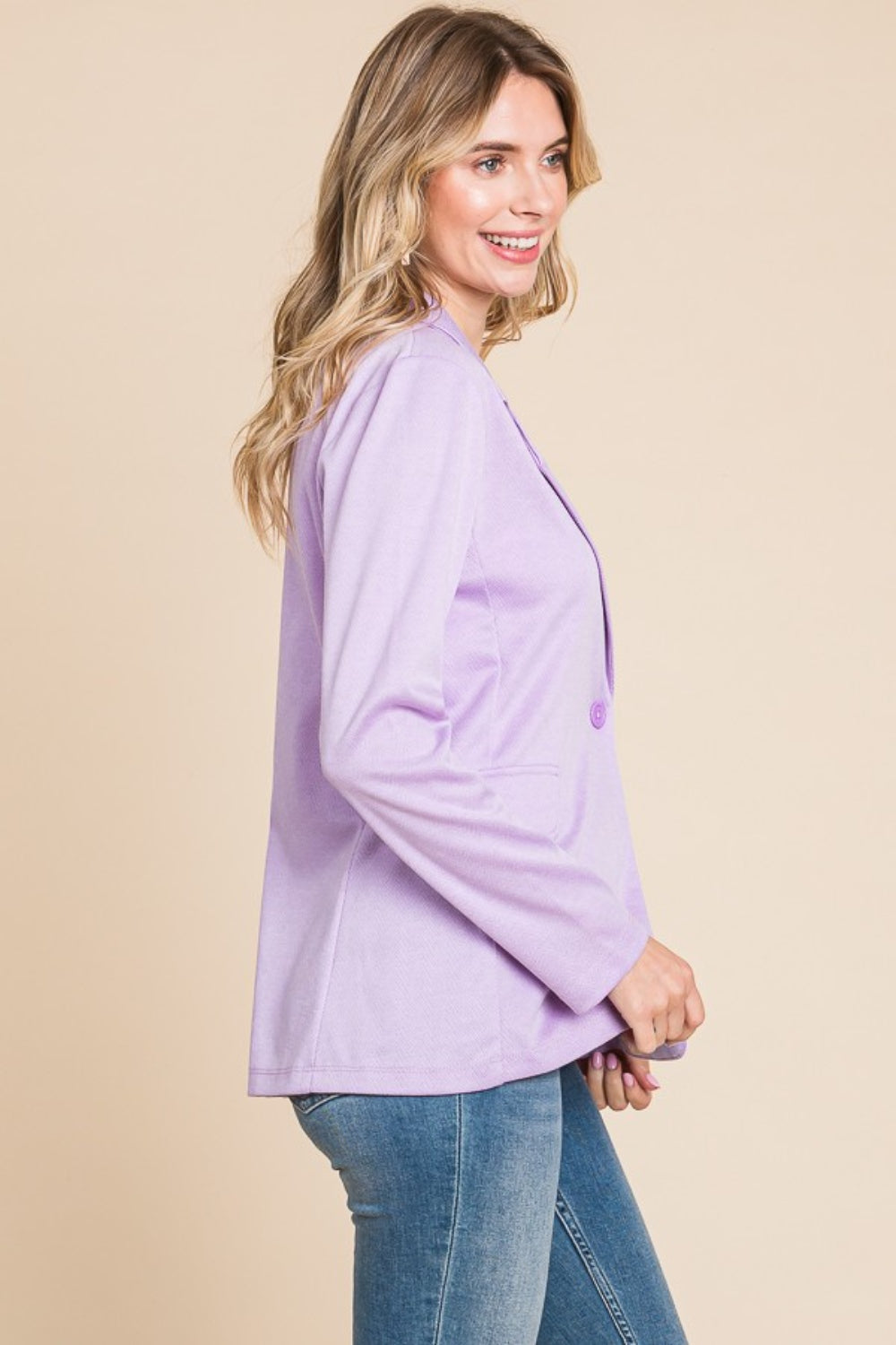 Woman wearing a button-up long sleeve slit blazer, light purple, in profile view, paired with jeans, showcasing basic style elegance.