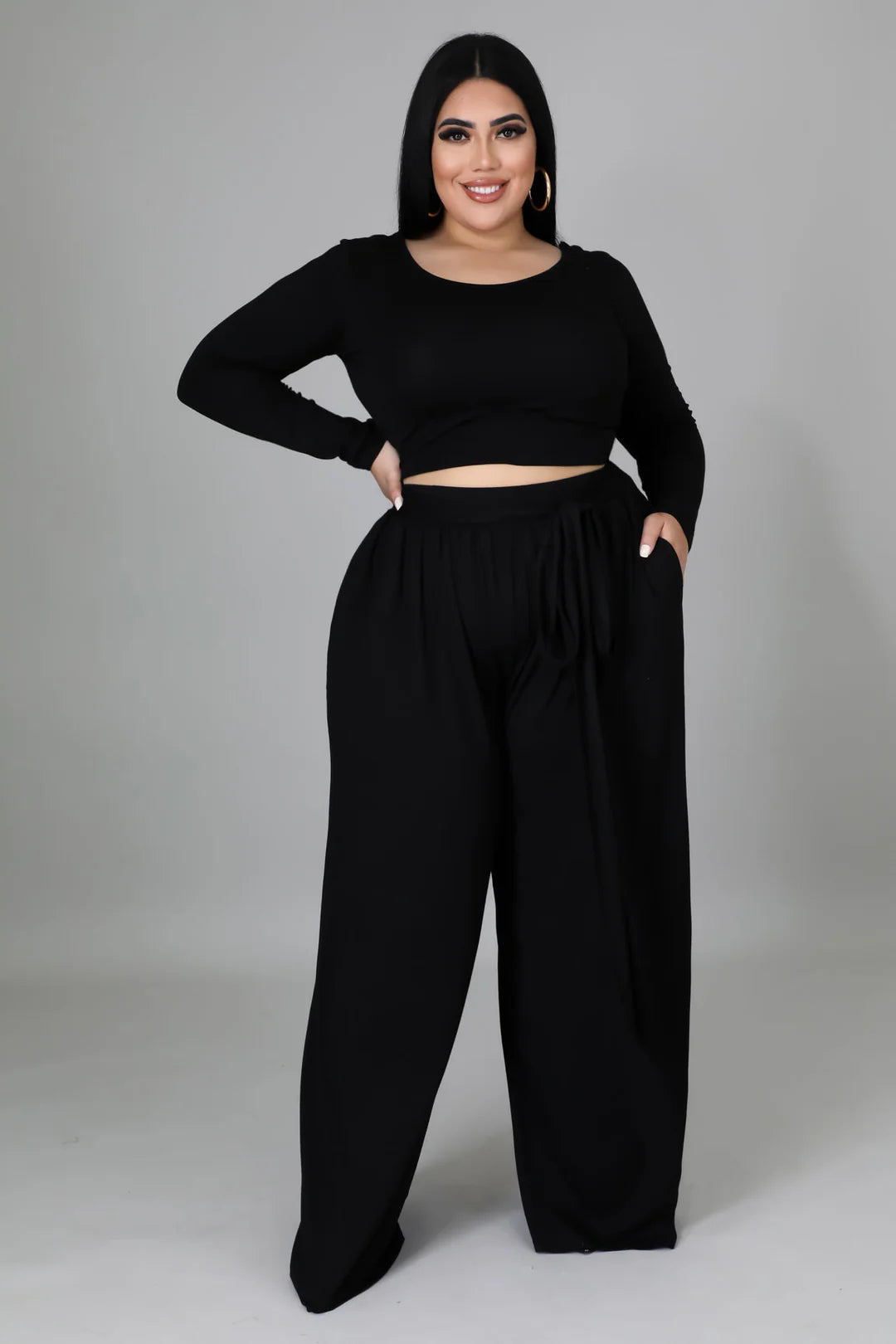 Woman wearing a chic black crop top and loose pants set with long sleeves, square neckline, and high-waisted fit with pockets.