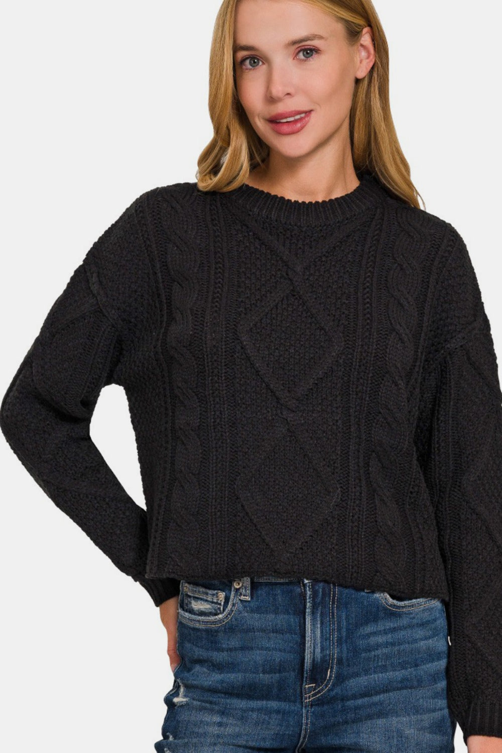 Woman wearing cropped black cable-knit sweater with high-low hem and side slits, paired with high-waisted jeans.