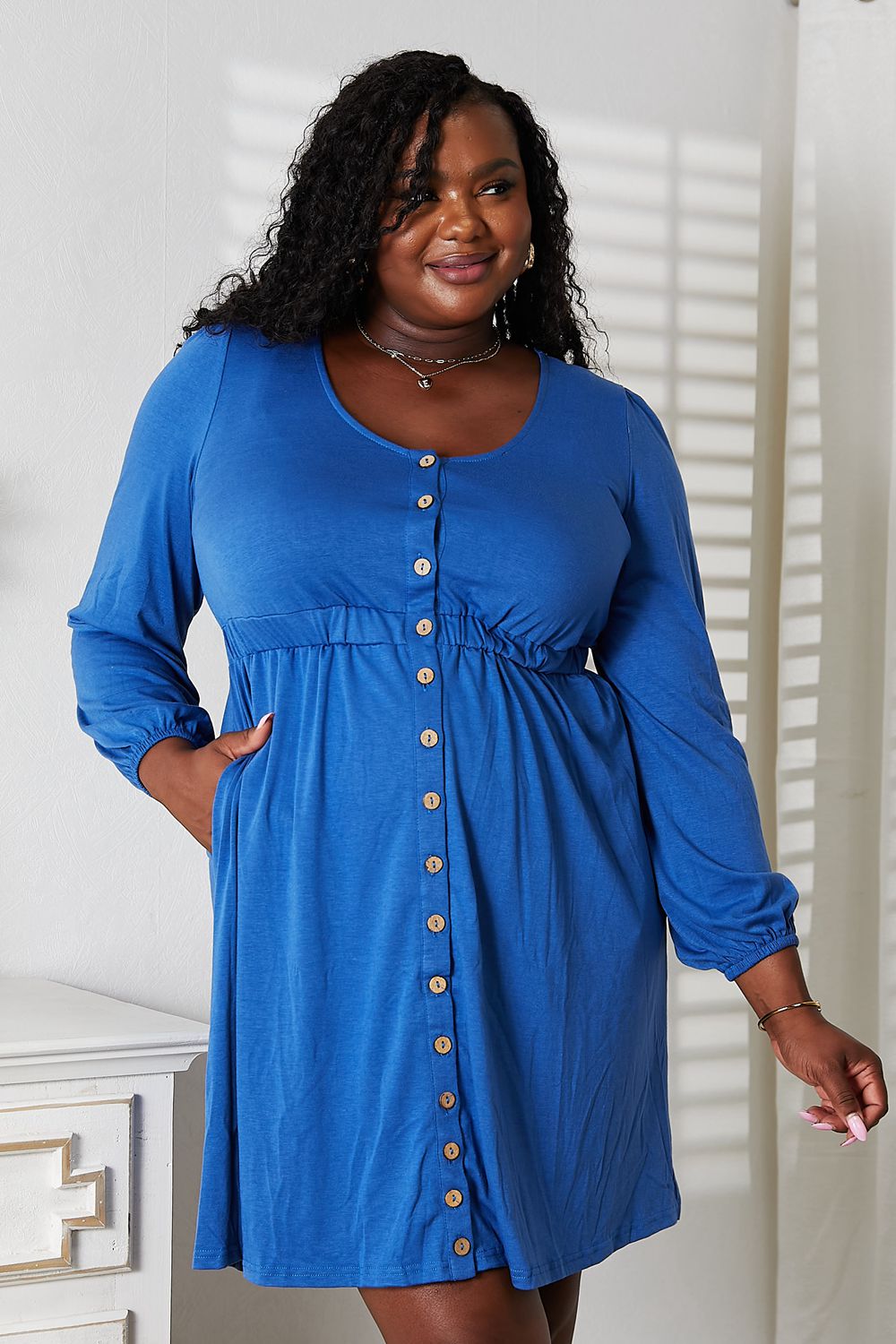 Woman in blue scoop neck empire waist dress with buttons, showcasing a chic and fashionable look.