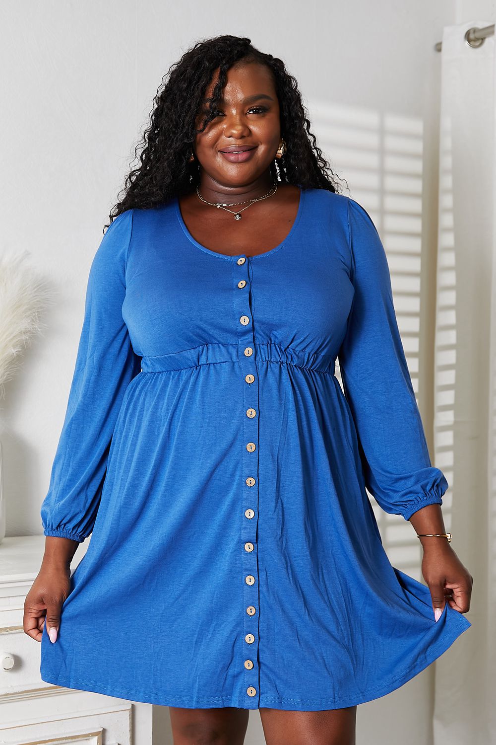 Woman wearing a blue scoop neck empire waist dress with decorative buttons and long sleeves, showcasing a chic and comfortable style.