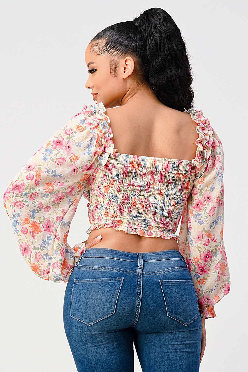 Woman wearing a chic floral sweetheart blouse with smocked body and long sleeves, in cream pink color, back view.