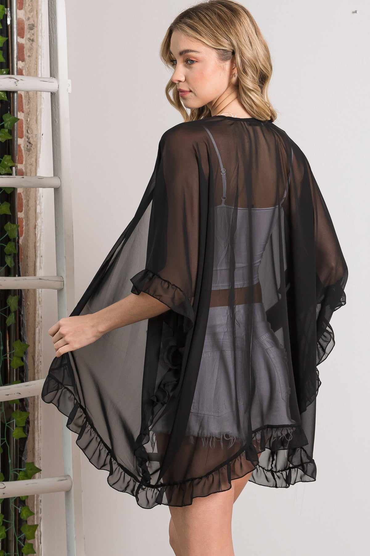 Black sheer shawl cardigan with ruffle accents, stylish and elegant lightweight outerwear made of 100% rayon, worn by a model.