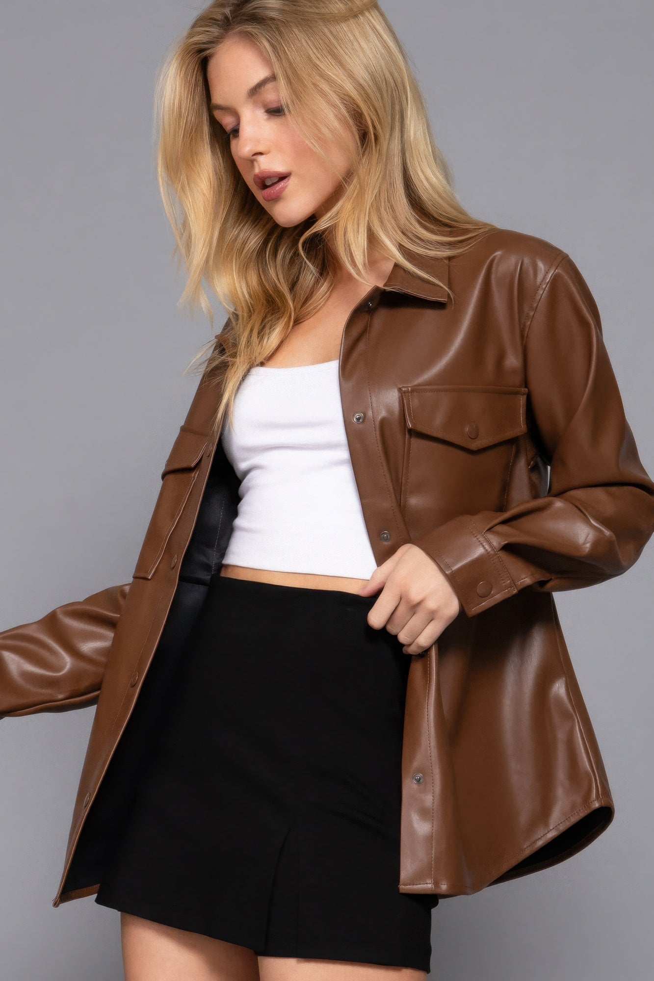 Woman wearing a chic brown faux leather shacket with long sleeves, styled over a white top and black skirt.