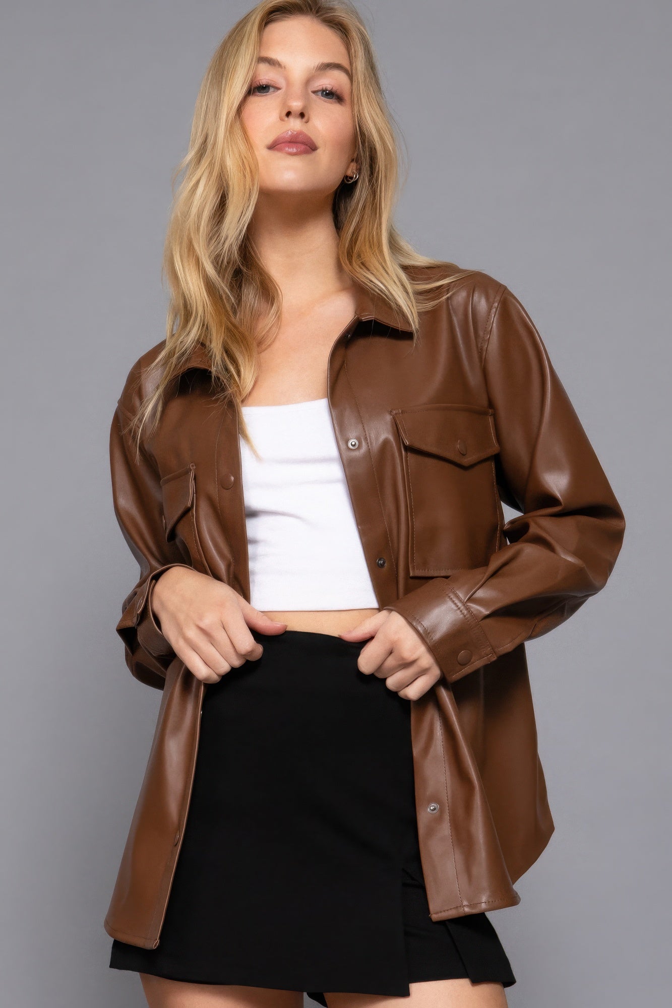 Woman wearing a chic faux leather shacket in brown, styled with a white top and black skirt, perfect for versatile layering.