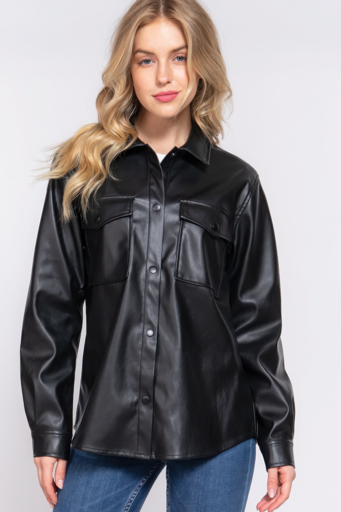 Woman wearing black long sleeve faux leather shacket with relaxed fit and button-up front.