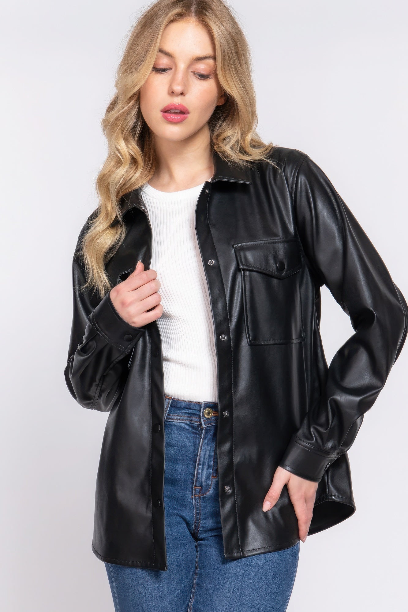 Woman wearing black long sleeve faux leather shacket over white top and jeans, showcasing chic and versatile style.