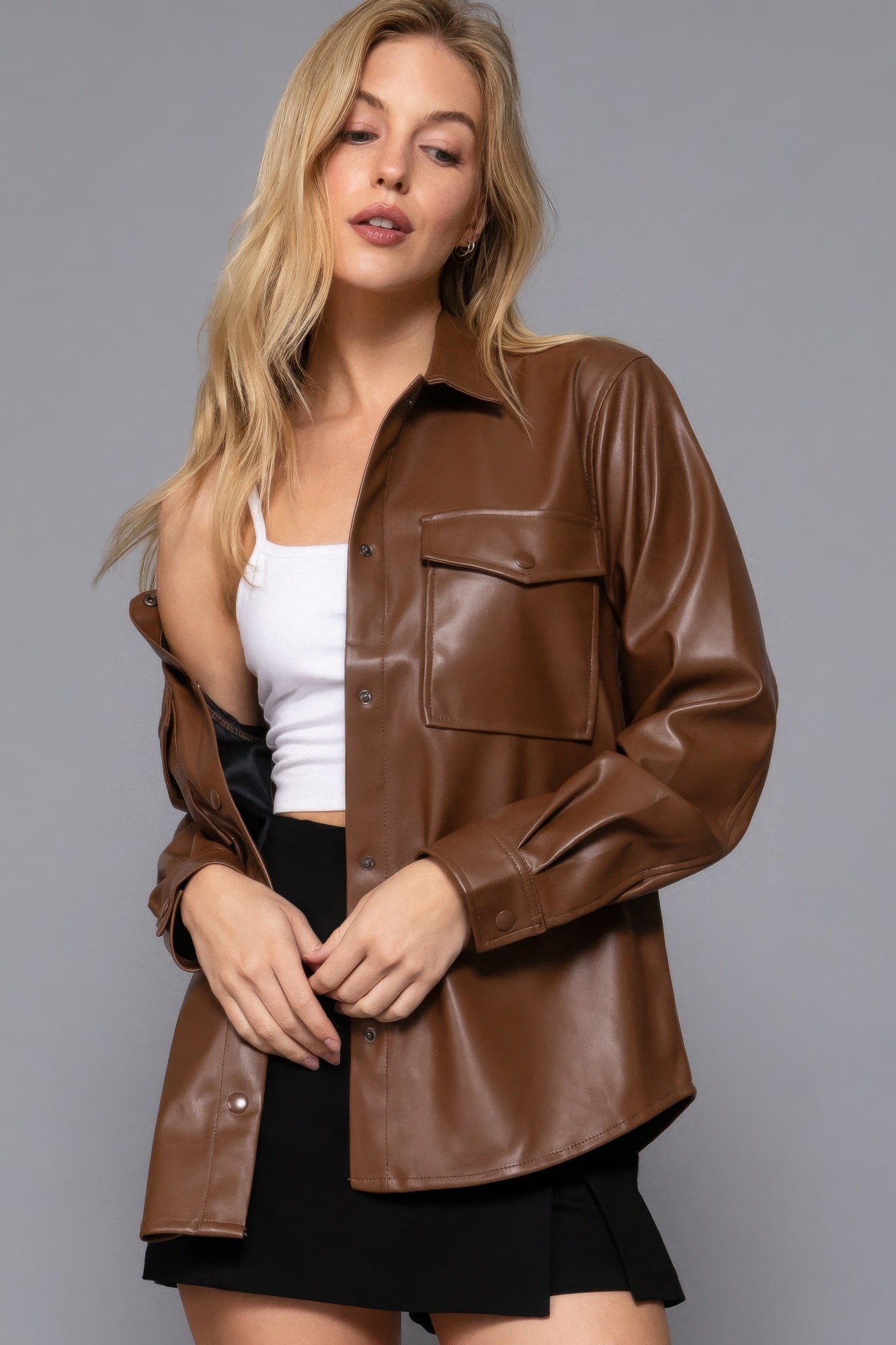 Woman wearing a chic brown faux leather shacket with long sleeves, styled over a white top and black skirt, perfect for layering.